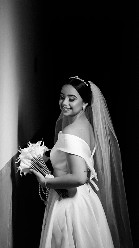 Noiva sorrindo com buquê de copos-de-leite, em preto e branco