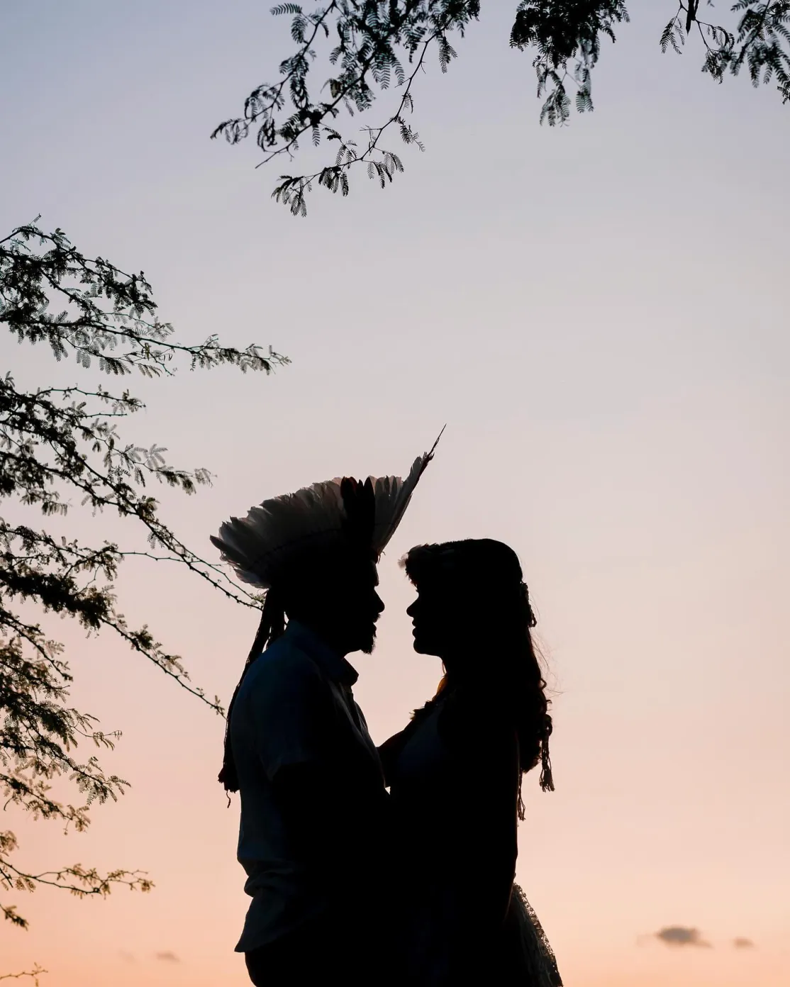 Silhueta de casal ao entardecer, com cocar indígena